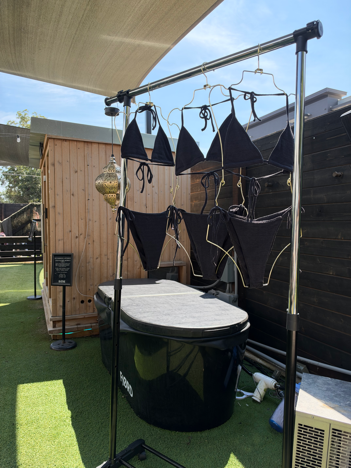 Black merino wool bikini tops and bottoms hanging on a rack beside a cold plunge tub and sauna